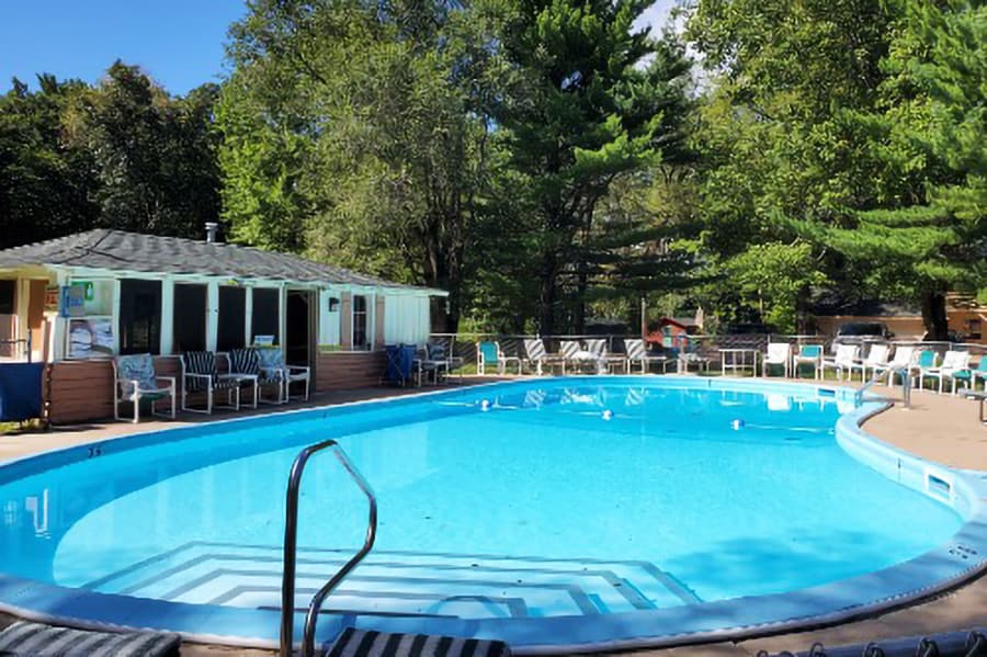 A clear swimming pool surrounded by lounge chairs and trees.
