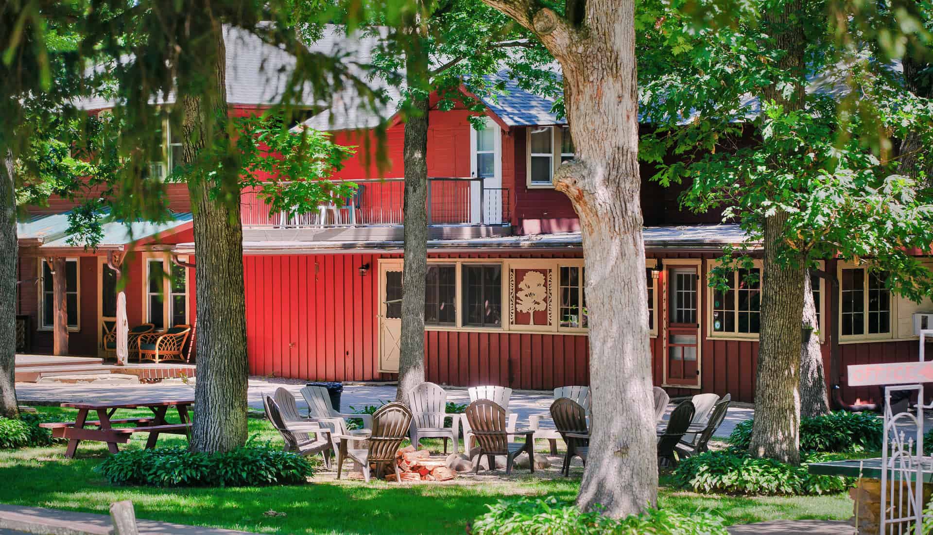 A cozy red lodge surrounded by green trees and outdoor seating.