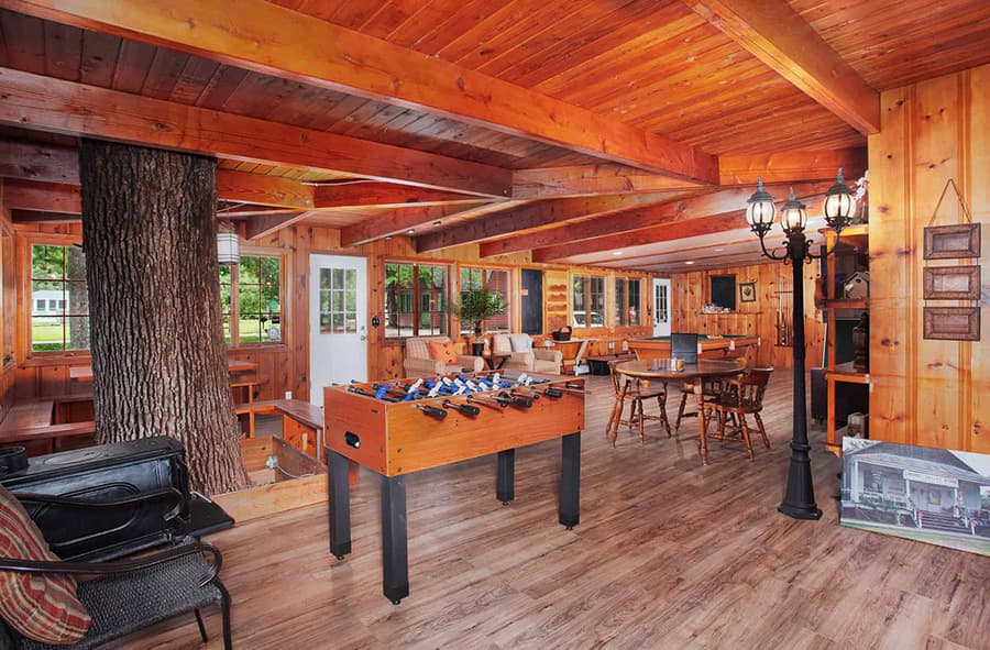 Bright, wooden interior of a game room featuring a foosball table, a tree, and casual seating.