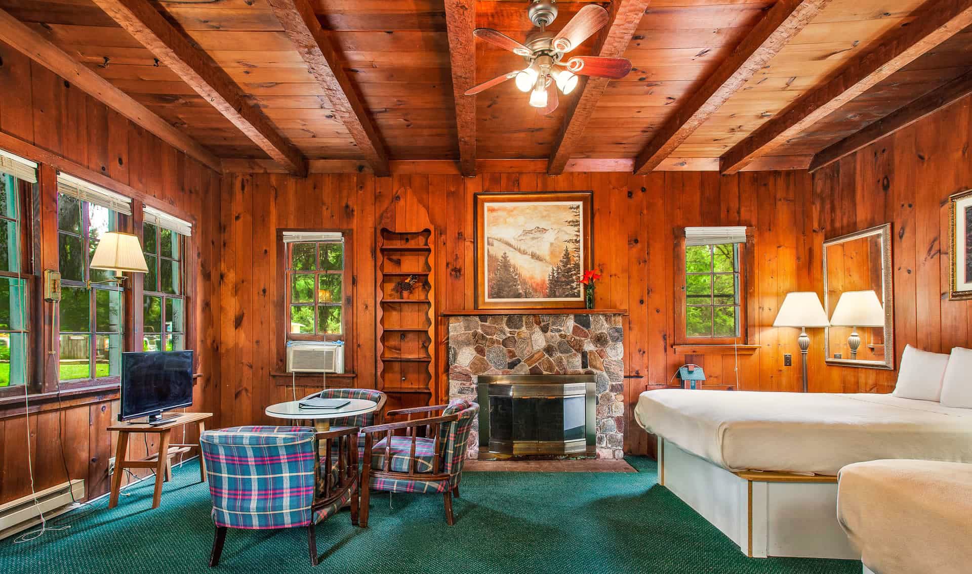 A cozy cabin interior featuring wooden walls, a stone fireplace, and a bed with plaid seating.