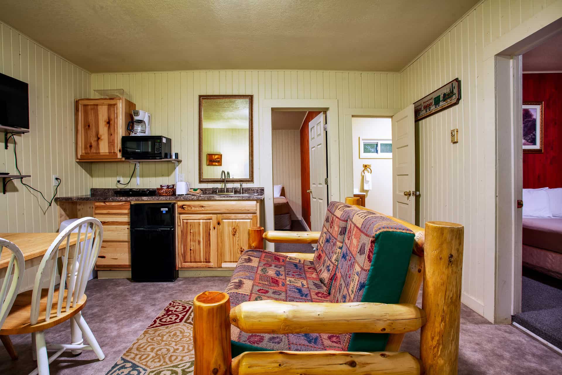 A cozy living area with rustic wood furniture, a small kitchen, dining area, and a rustic log sofa.