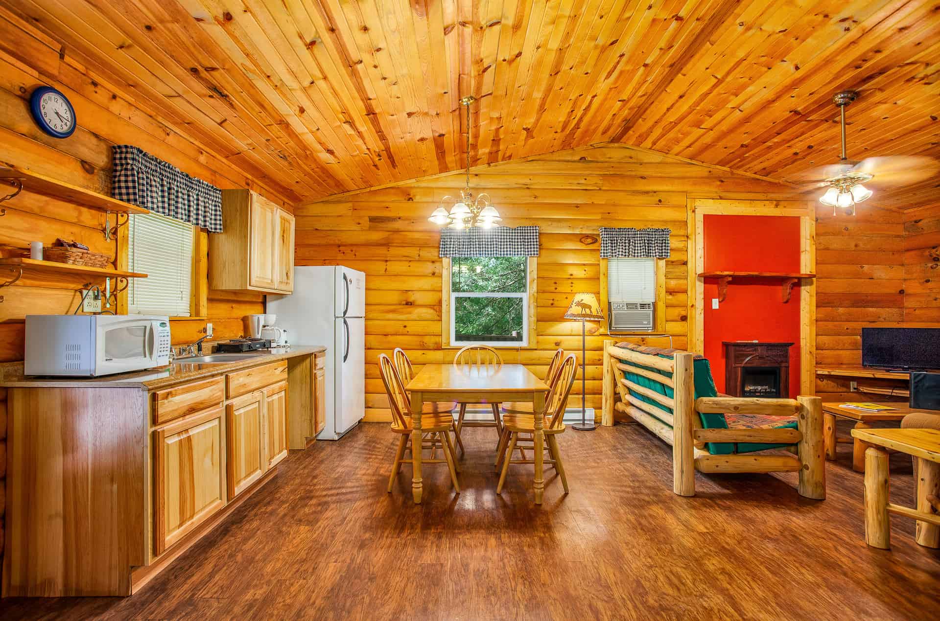 A spacious, rustic log cabin interior with a full kitchen, a dining area, and a cozy living space featuring a fireplace and wooden furniture.
