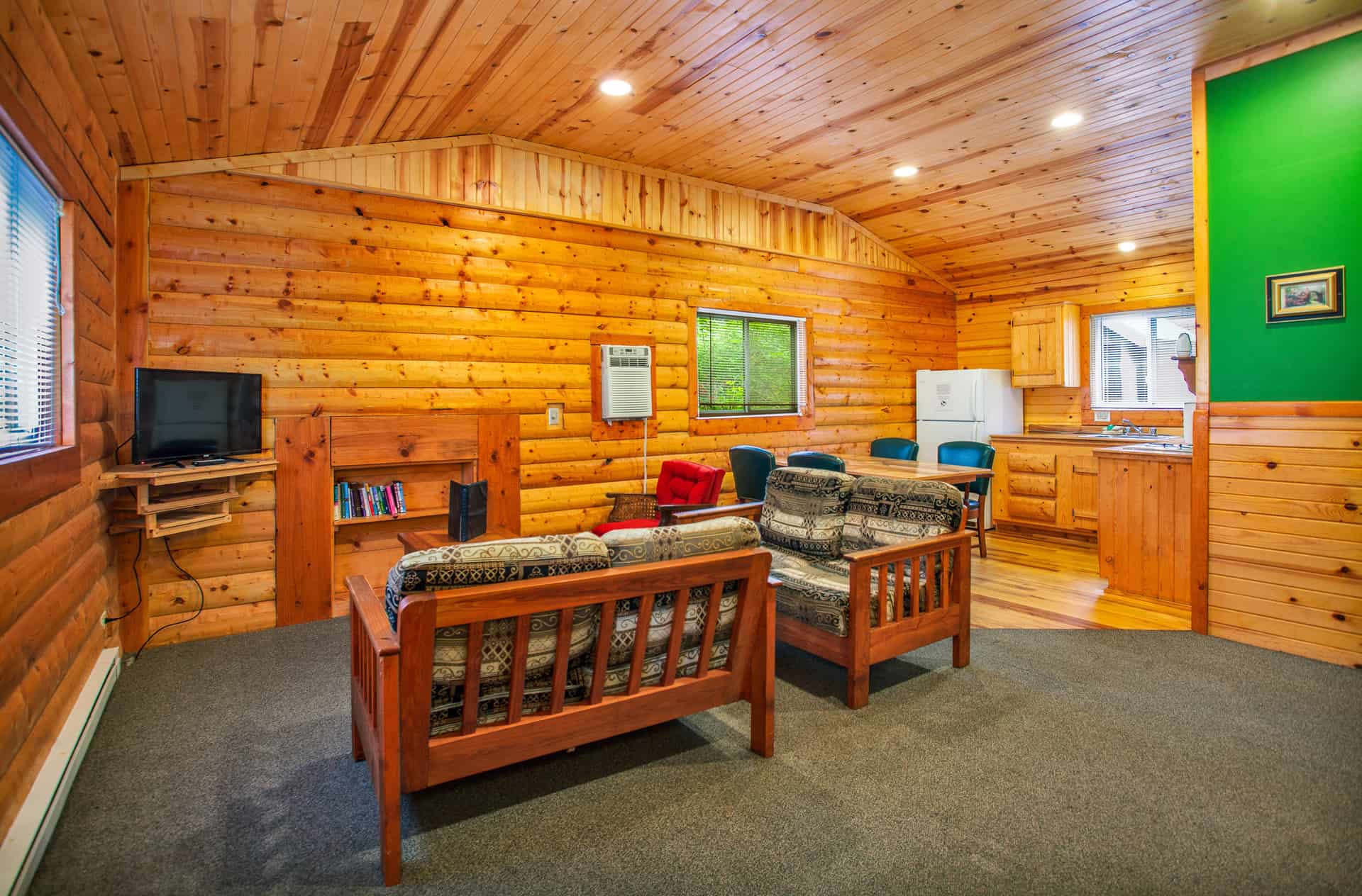 A warm, inviting common area in a log cabin with polished wood walls, a fireplace, comfortable seating, and a small dining or work area.