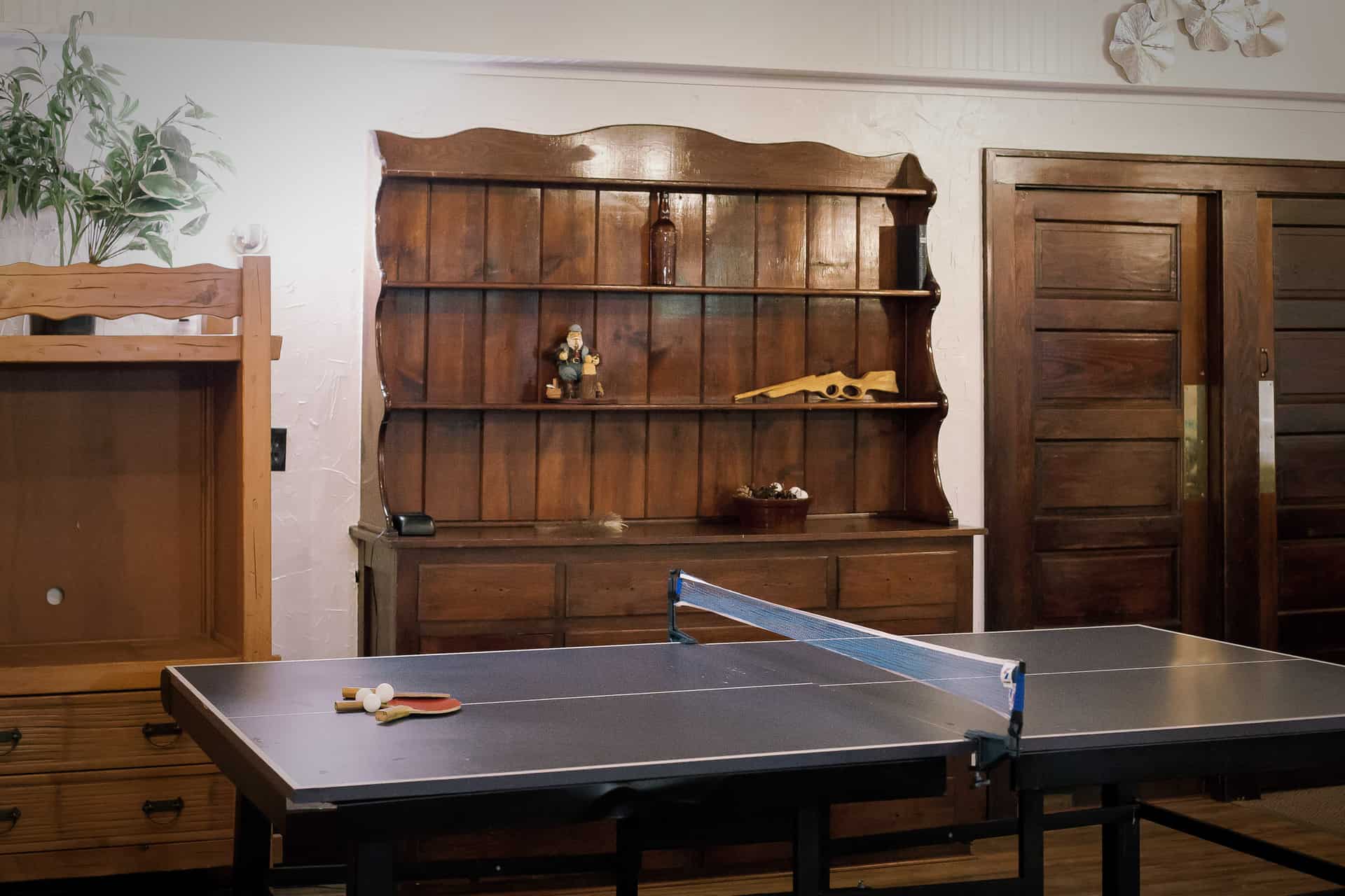 A recreational area with a ping pong table in the foreground, and a large wooden hutch and built-in shelves in the background.