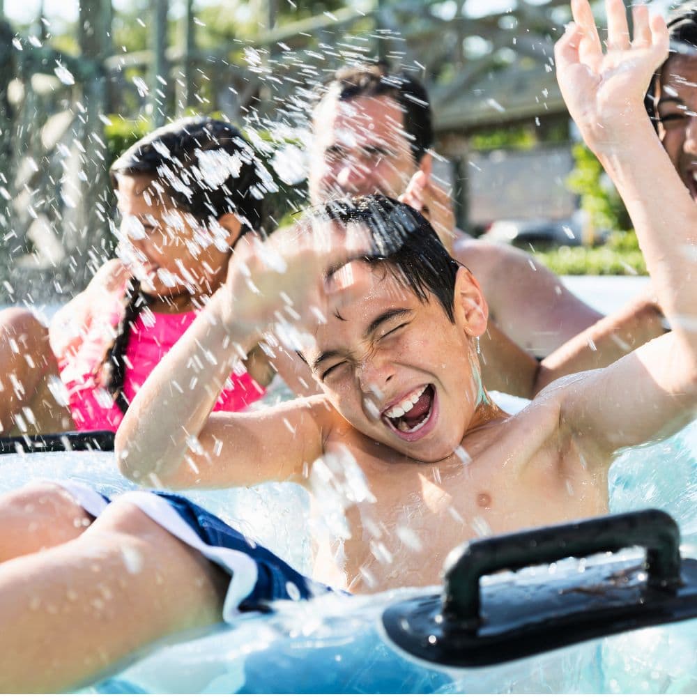 A young boy joyfully splashes water while riding on a float with friends.