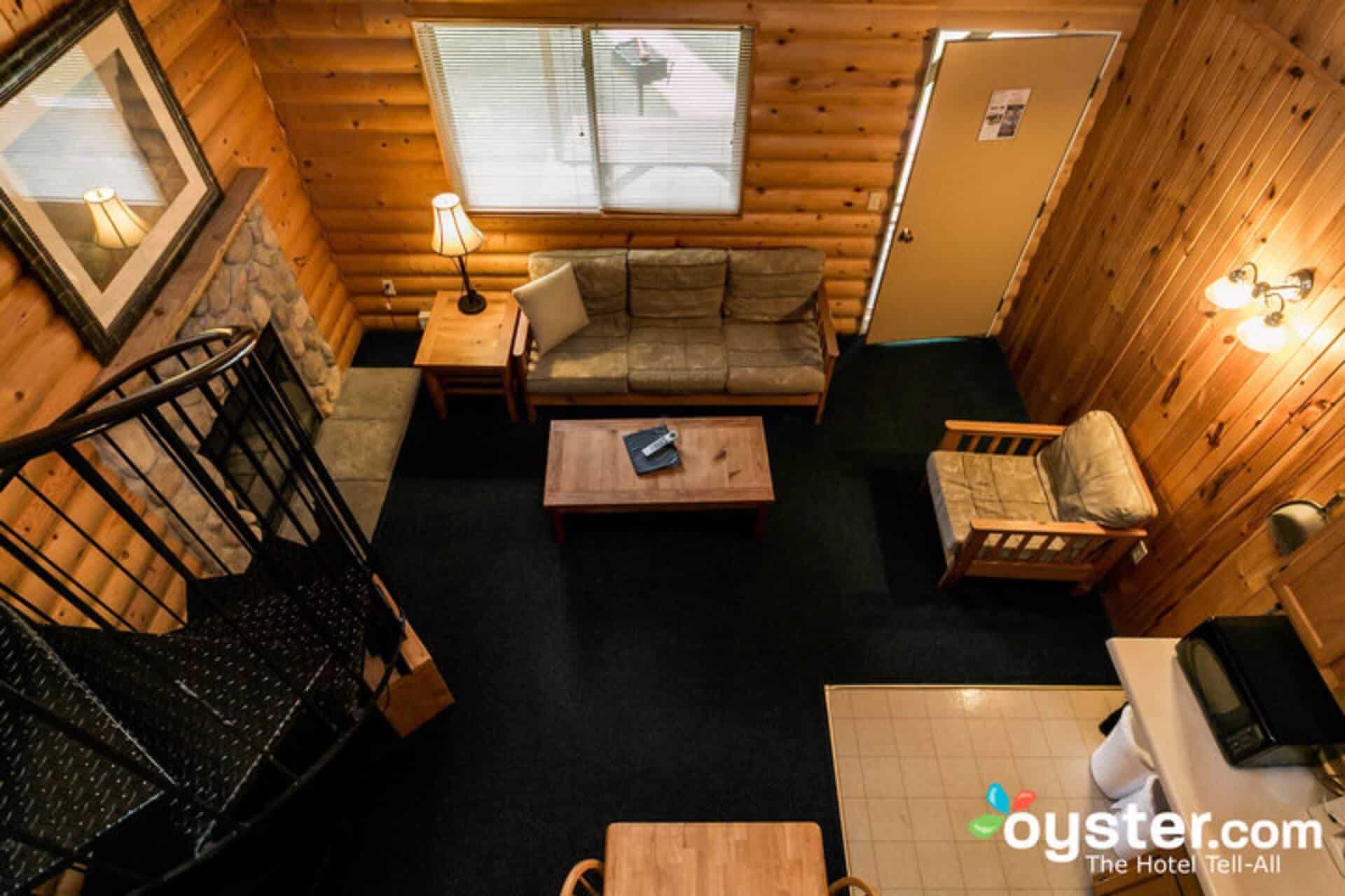 A bird's eye view of a cabin living space with wood-paneled walls, featuring a spiral staircase, sofa, coffee table, and dark carpet.